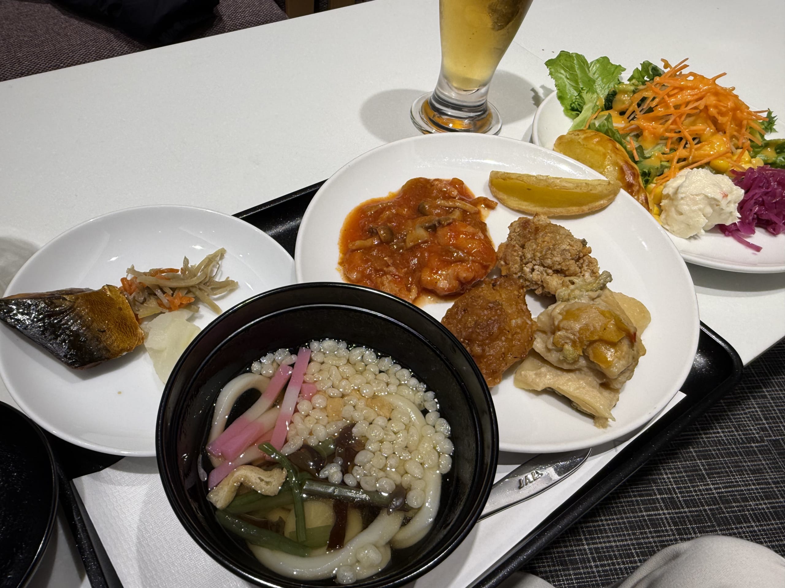 Tray with beer, udon, and various buffet foods.