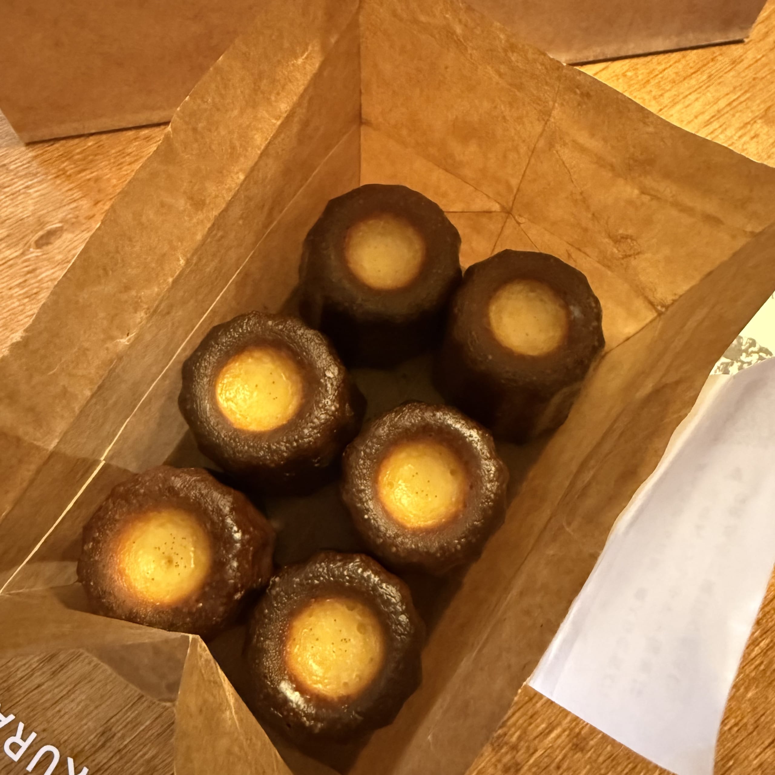 6 baked caneles in a kraft box.
