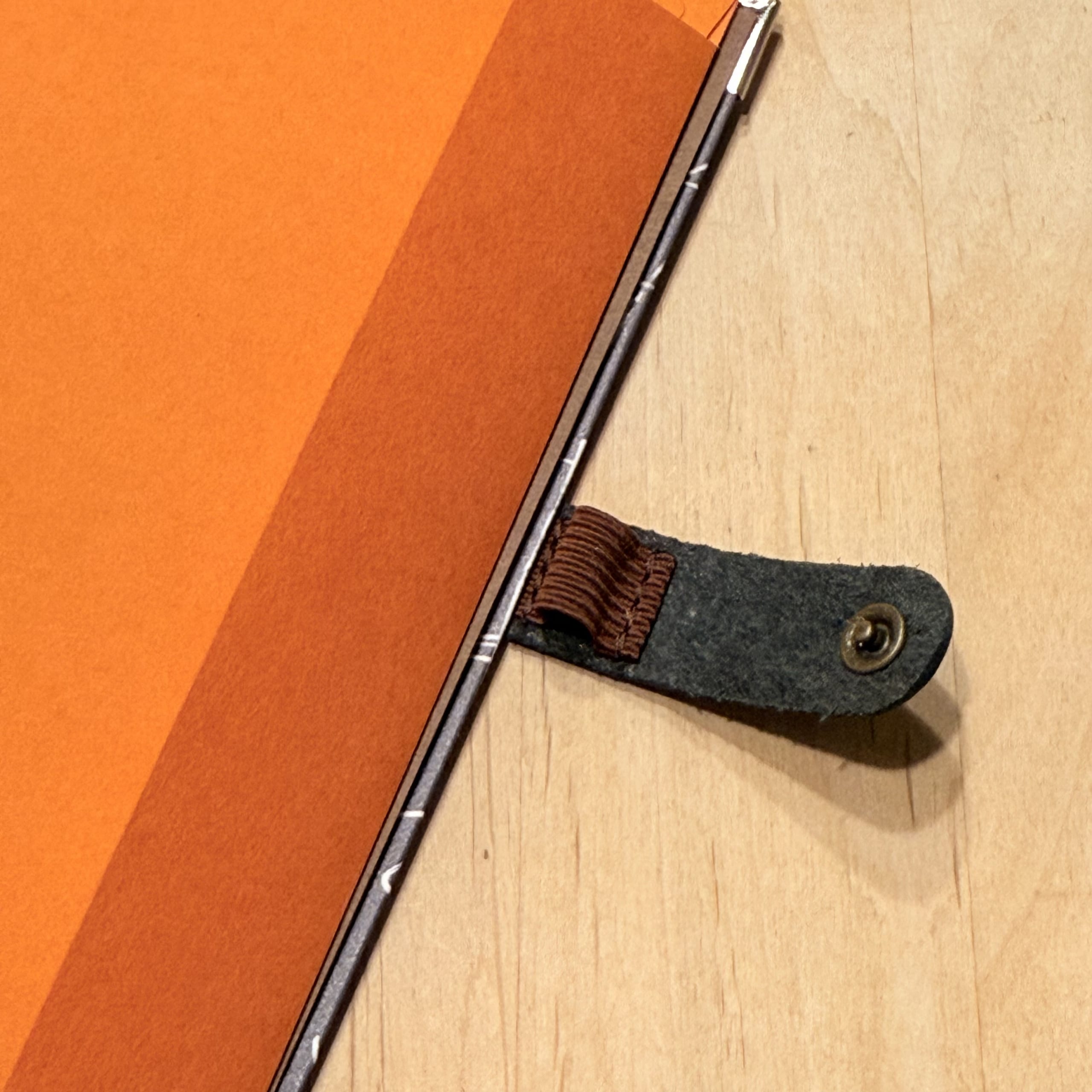 Orange notebook and leather pen loop on a desk.