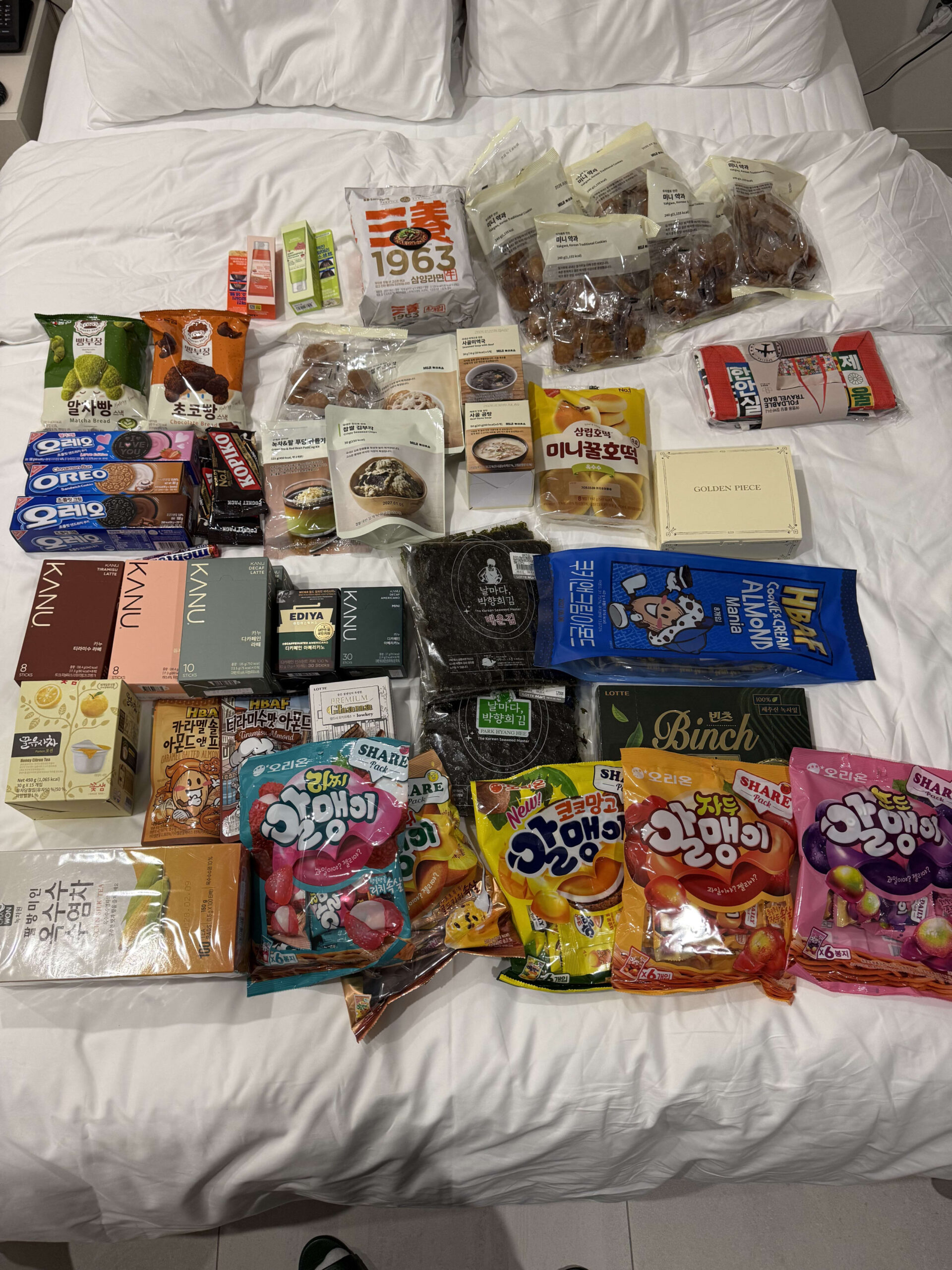 Korean souvenirs like snacks, coffee, and seaweed on a bed.
