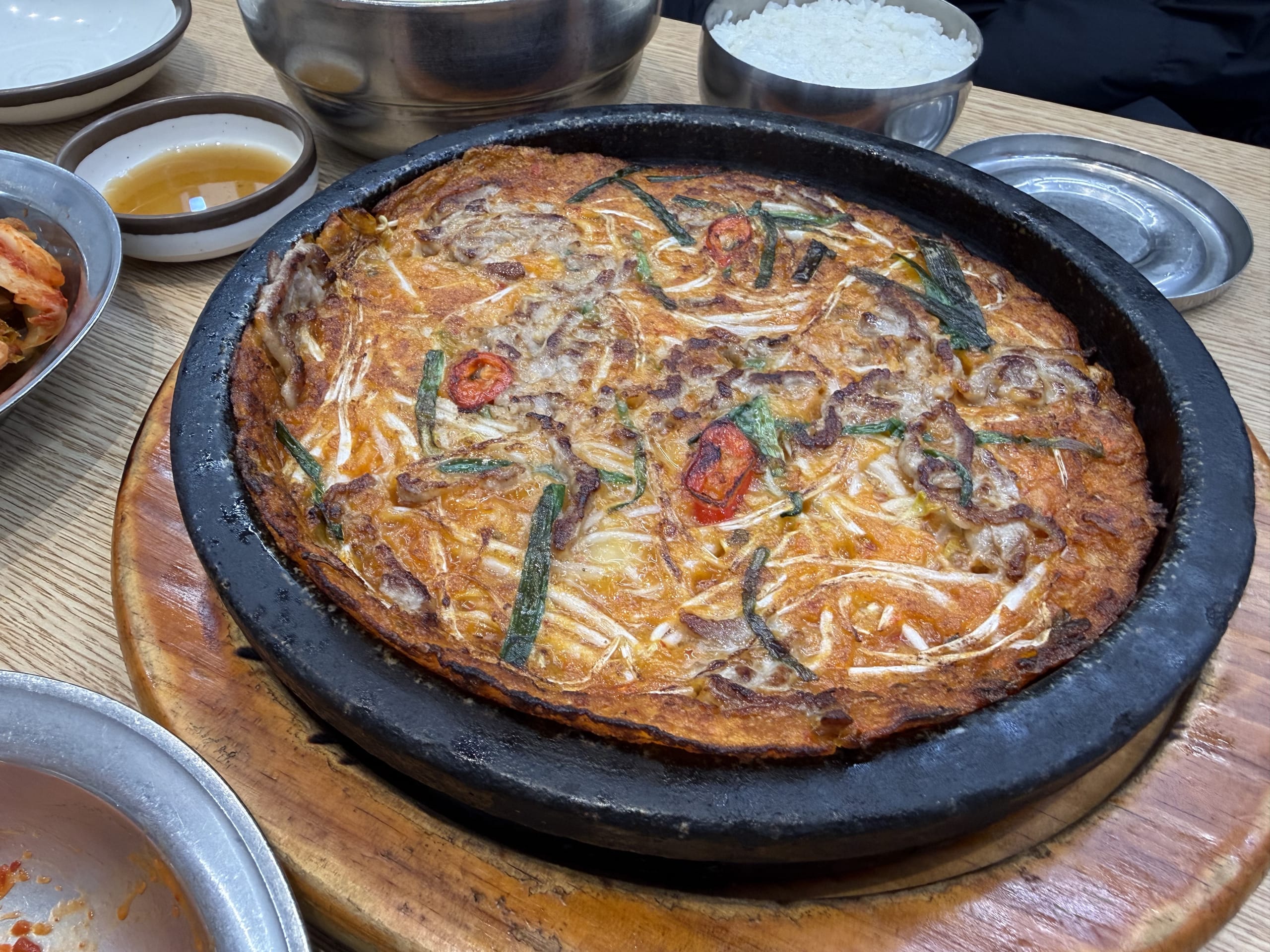 Sizzling Korean pancake on a hot black plate with side dishes.