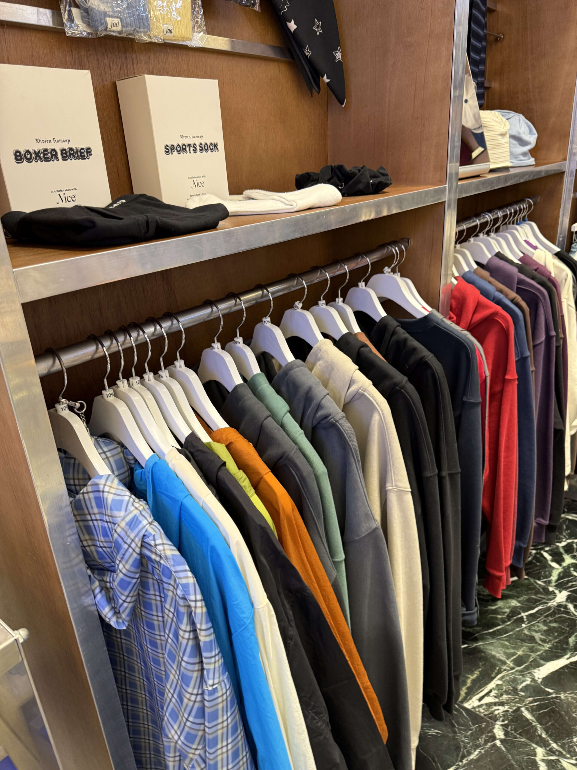木目調棚に並ぶ色鮮やかな服と上段の白い靴下箱。