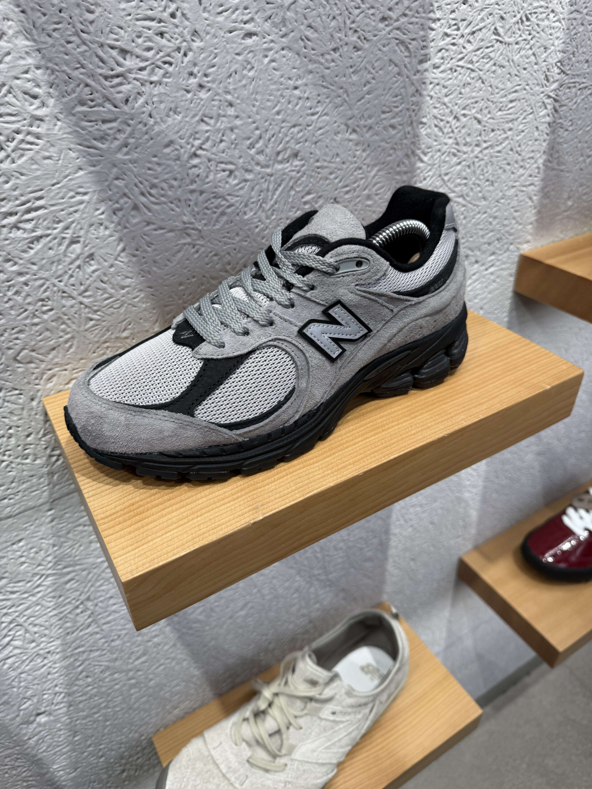 Grey New Balance mule sneaker on a wooden shelf against a white wall.