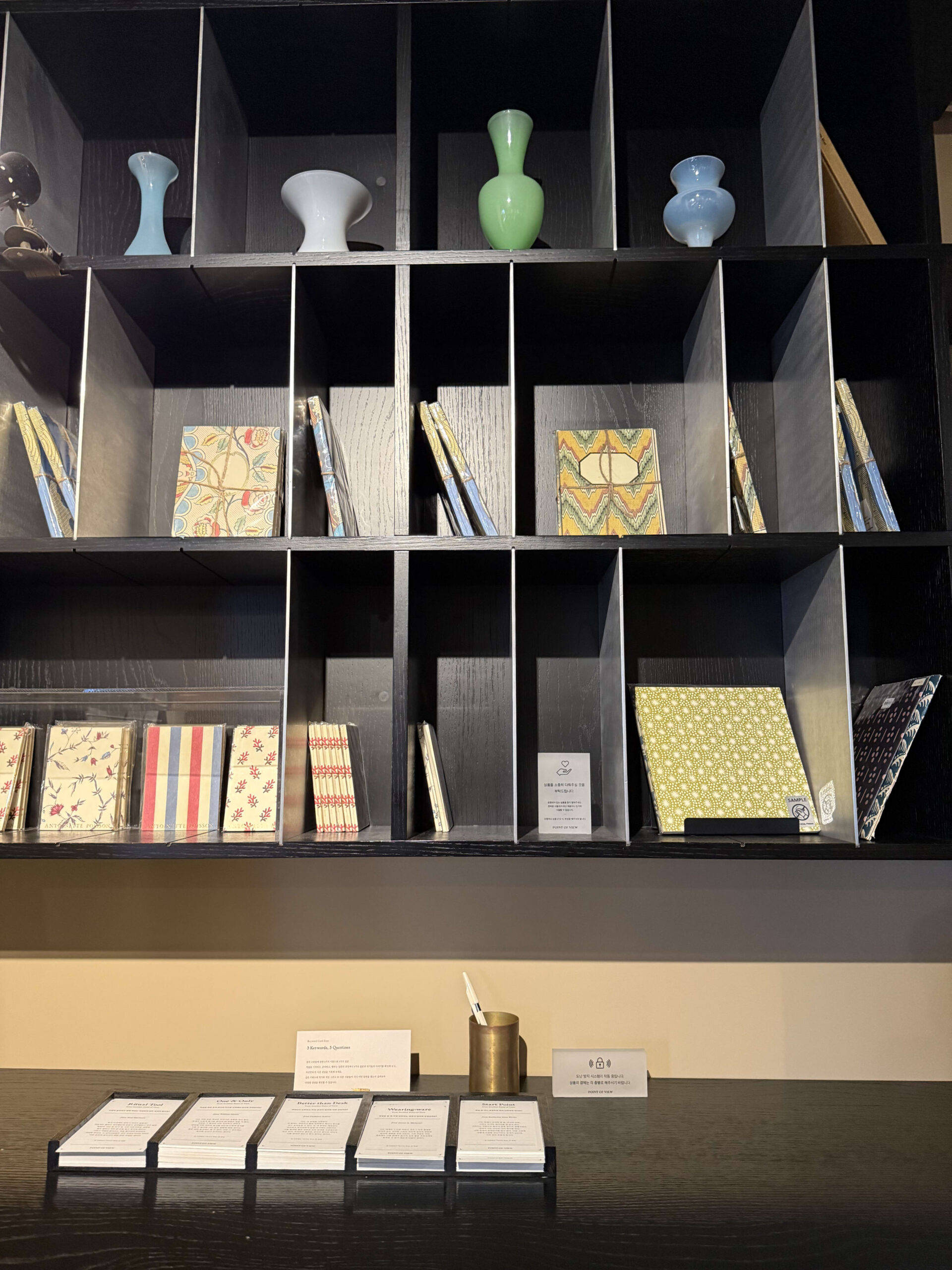Patterned notebooks and vases on a black shelf.