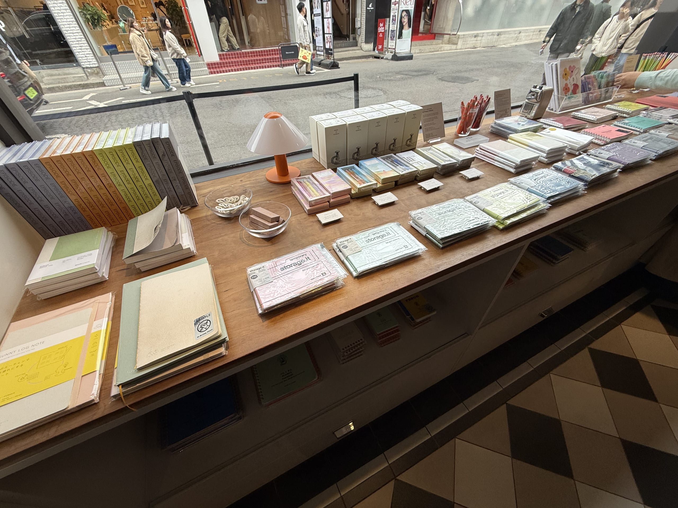 Colorful notebooks and stationery arranged on a wooden table by a window overlooking a Seoul street.