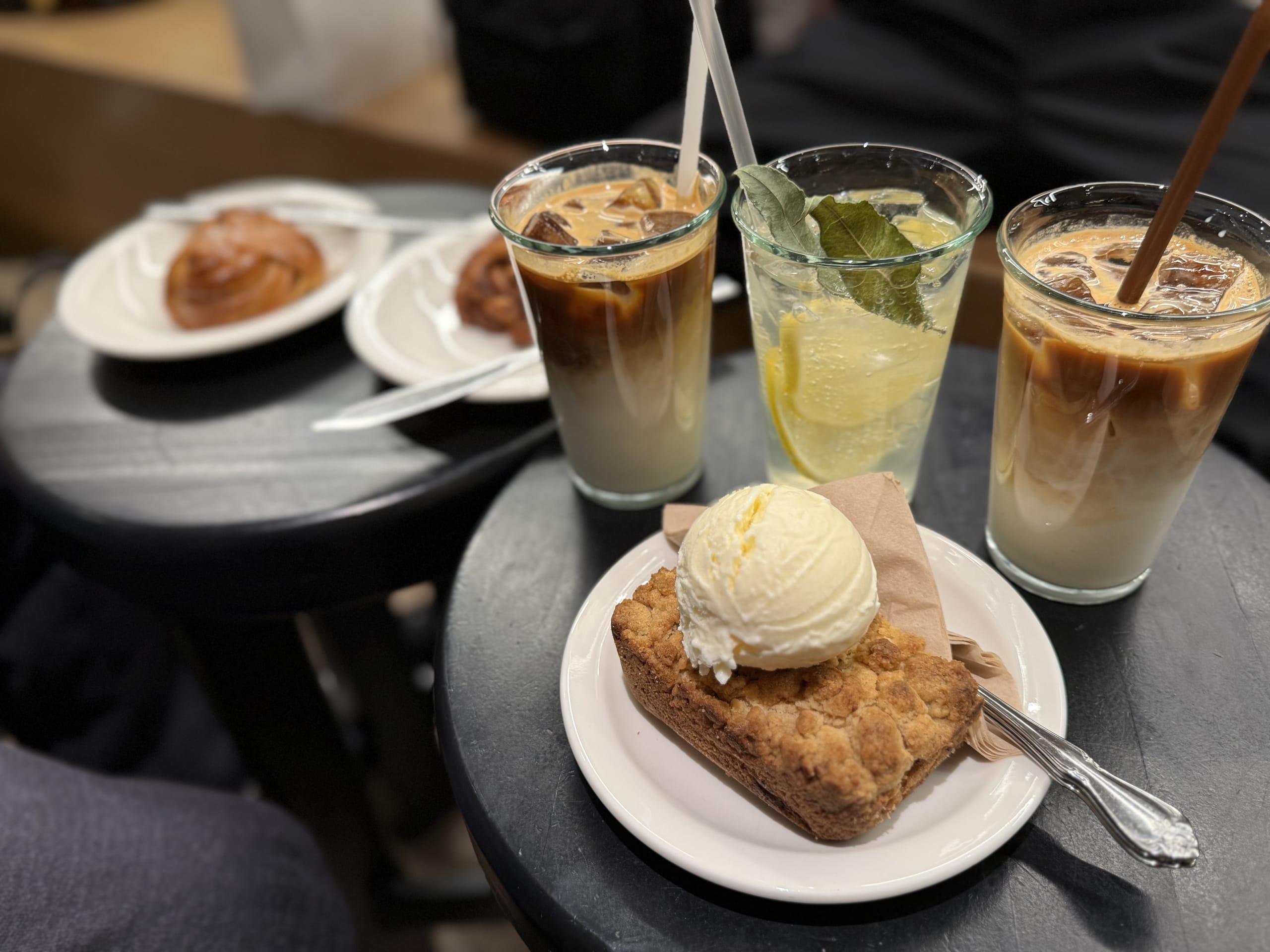 Lattes, lemonade and desserts on a black table.