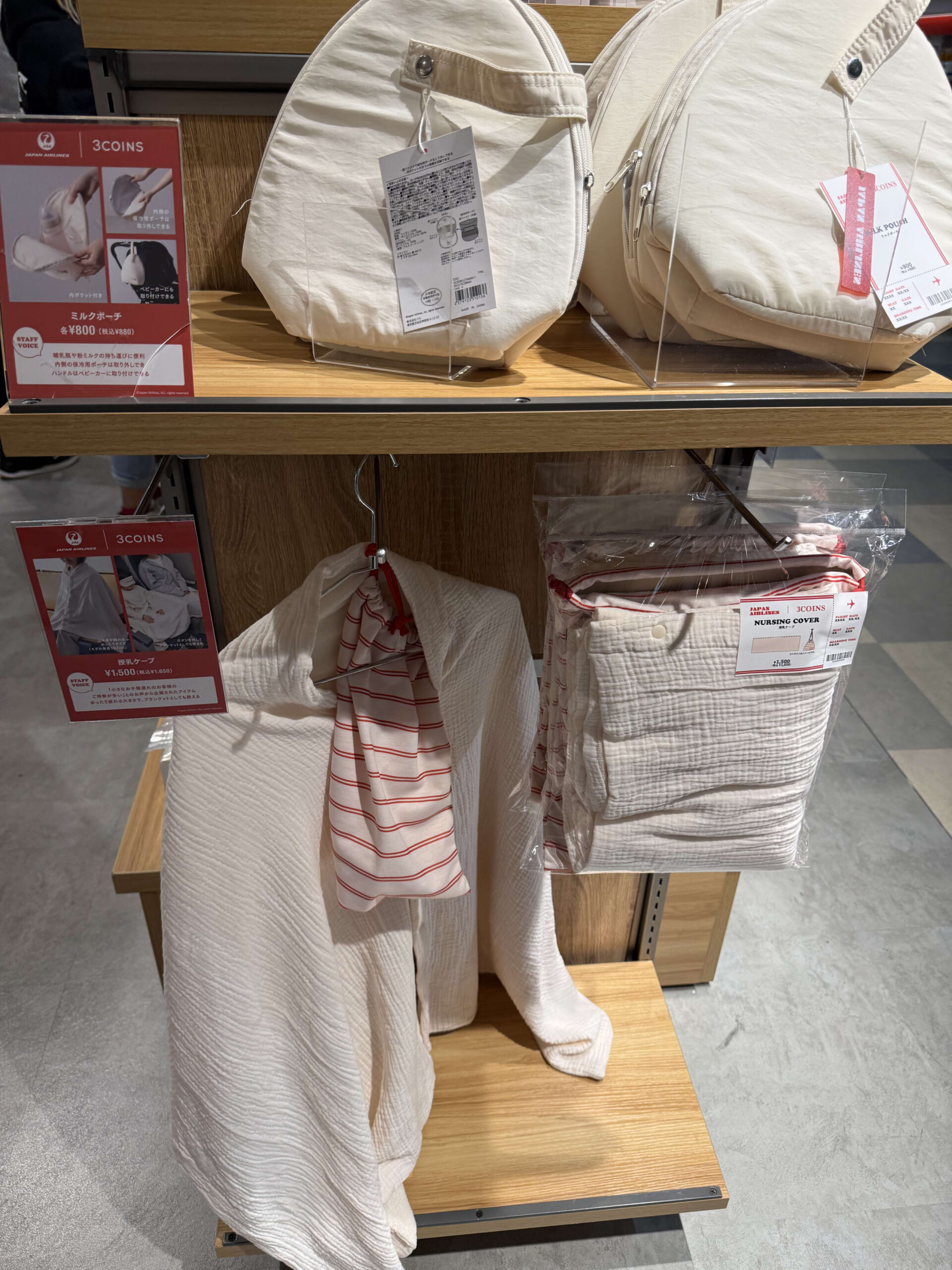 3COINSとJALコラボのミルクポーチと授乳ケープが木製の棚に並ぶ様子。