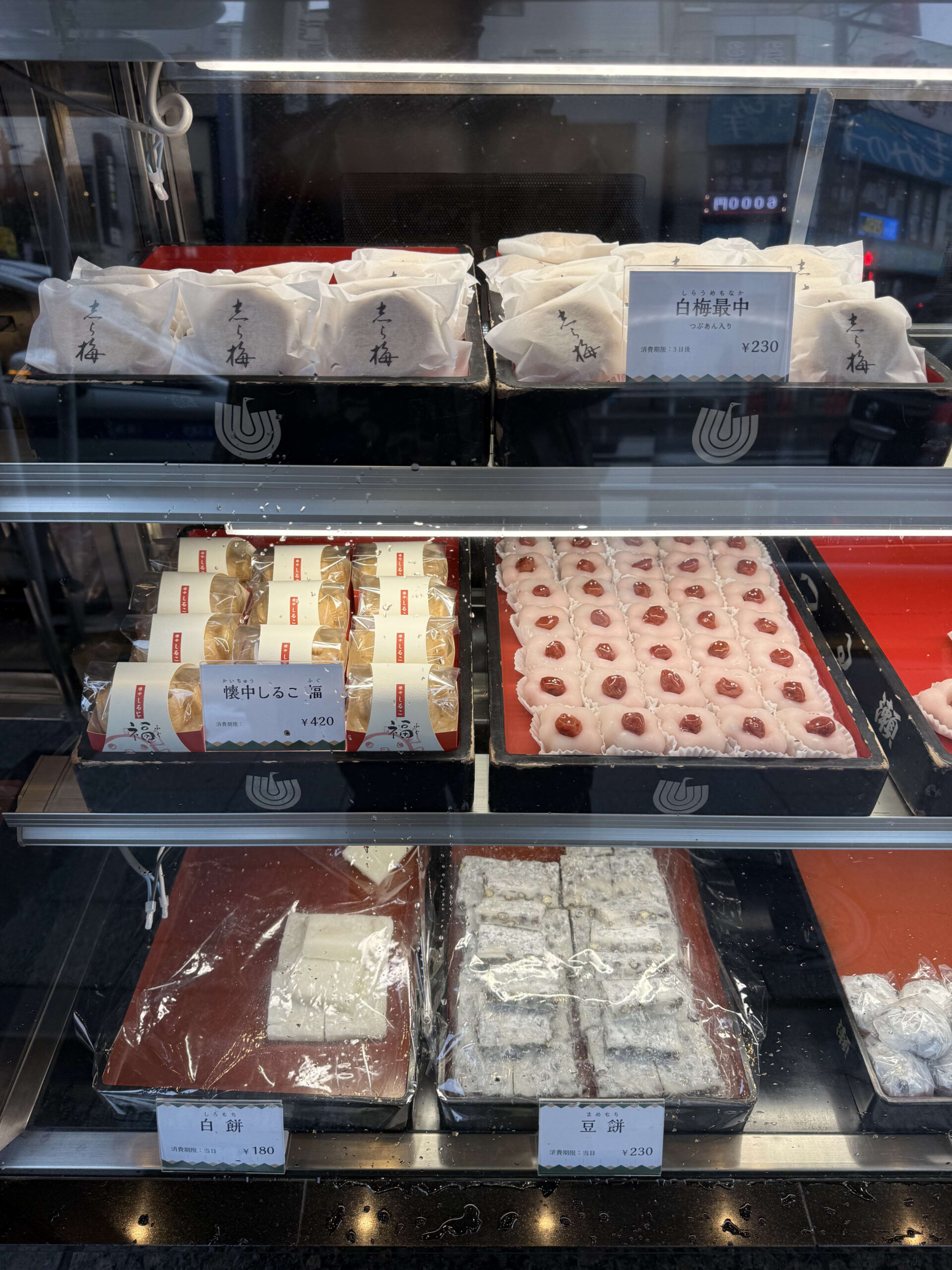 雨粒のつくガラスケースに並ぶ白梅最中や豆餅などの和菓子