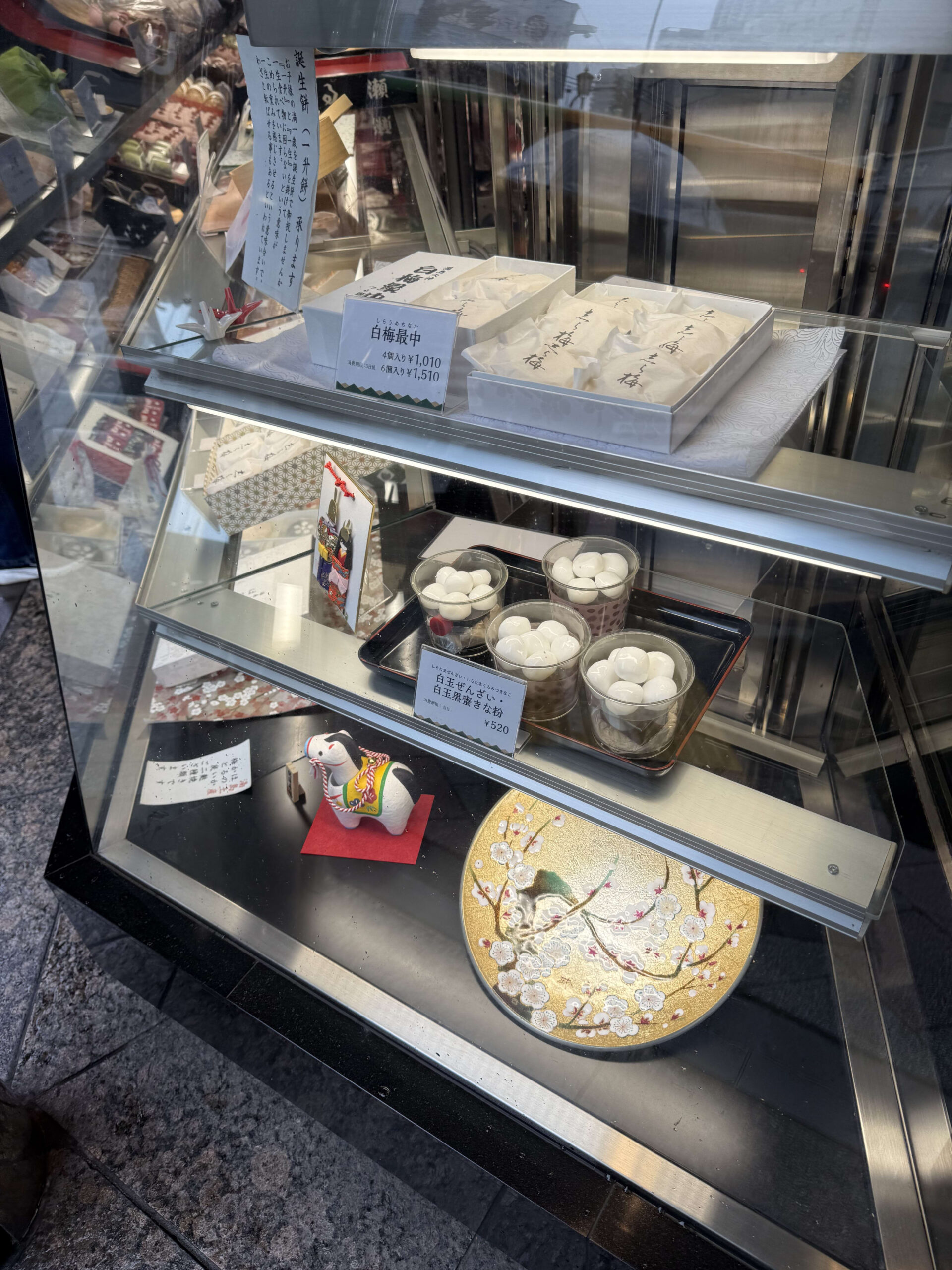 老舗和菓子店のショーケースに並ぶ白玉ぜんざいと最中、和の飾り。
