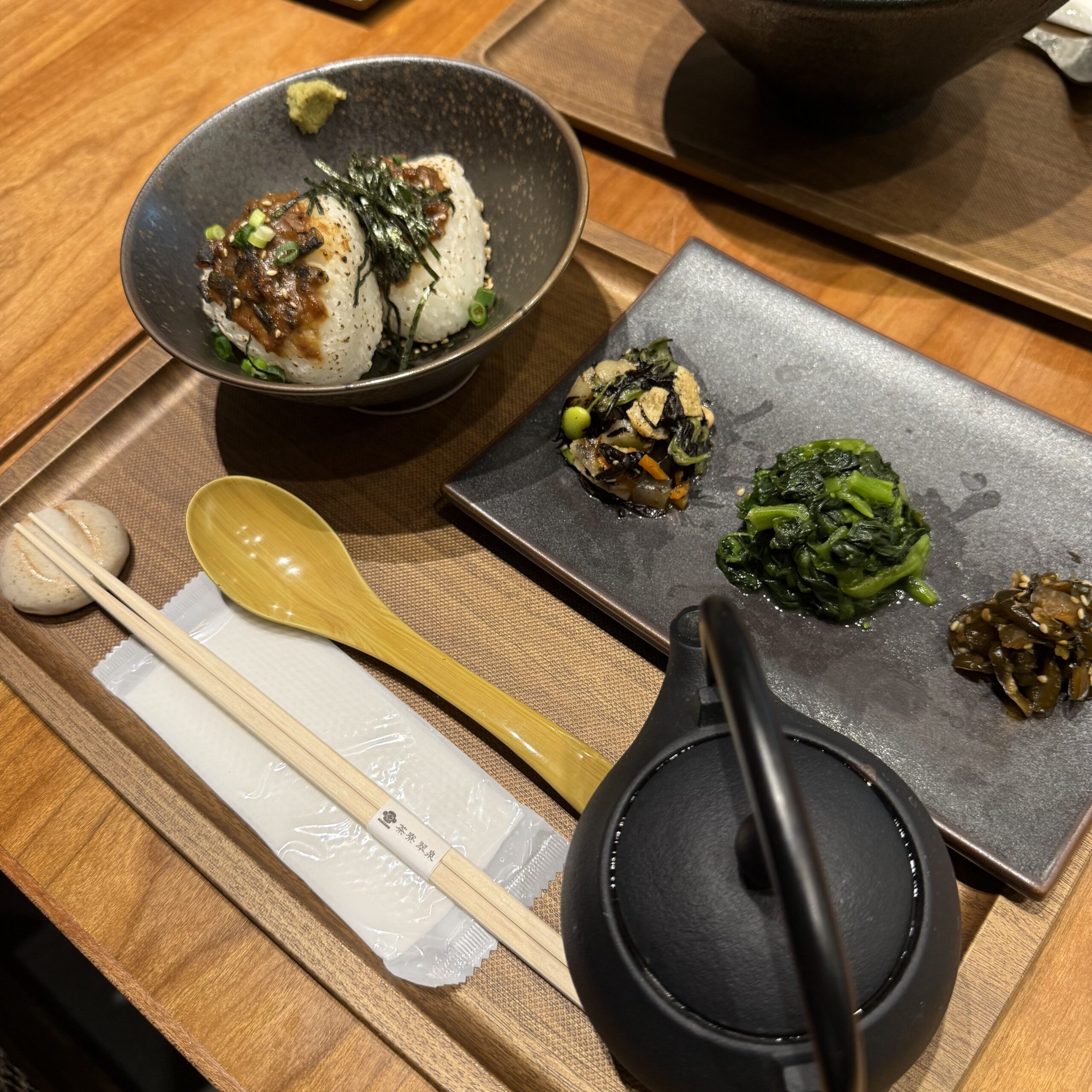 木製トレイの上の焼きおにぎり、3種のおばんざい、鉄瓶、木のスプーンと箸。
