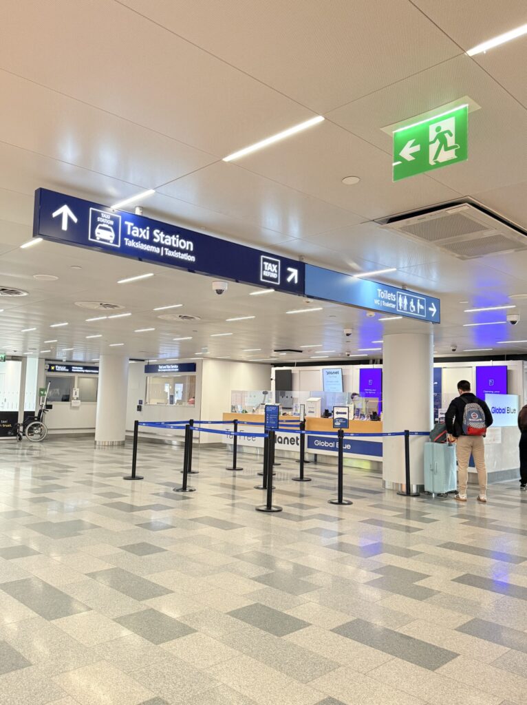 ヘルシンキ空港到着ロビーの免税カウンターと案内看板。