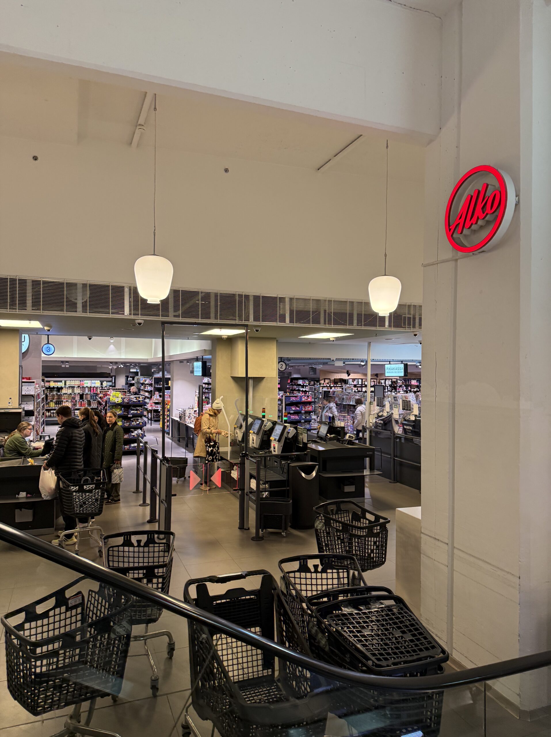 フィンランドの酒類専売店「Alko」の赤いネオンサインと整然と並ぶ黒いショッピングカート