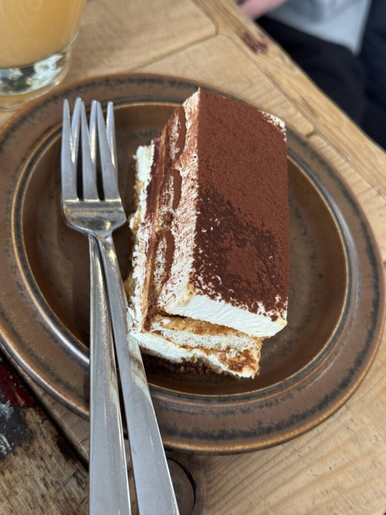 A square portion of classic tiramisu dusted with cocoa powder on a brown plate.