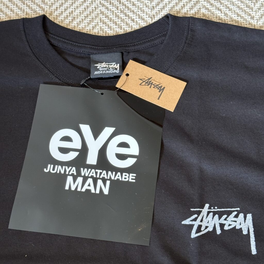 Close-up of the large black eYe tag and the Stussy paper tag on the collar