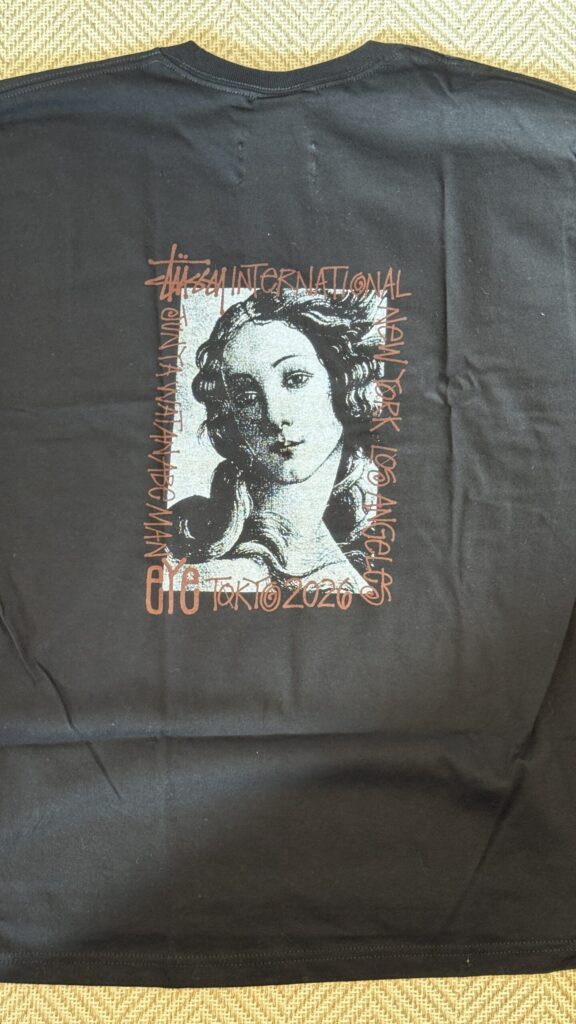 The back of a black t-shirt featuring a graphic of the eYe JUNYA WATANABE MAN x Stüssy collaboration. Text logos