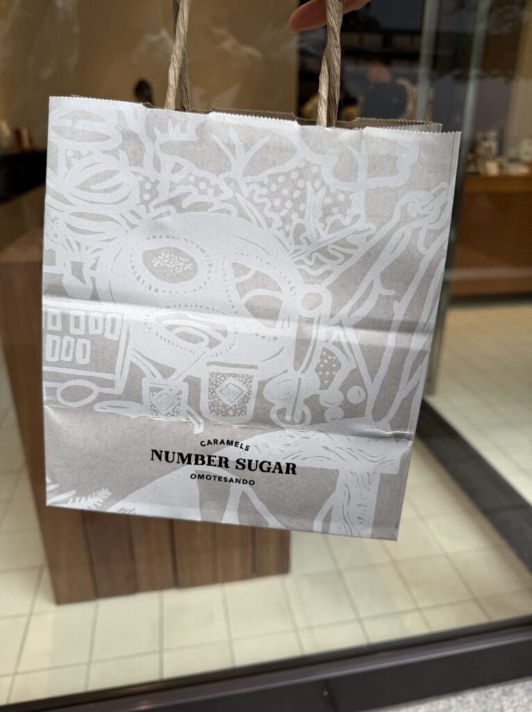 Craft paper bag with botanical white ink illustrations held against the shop window
