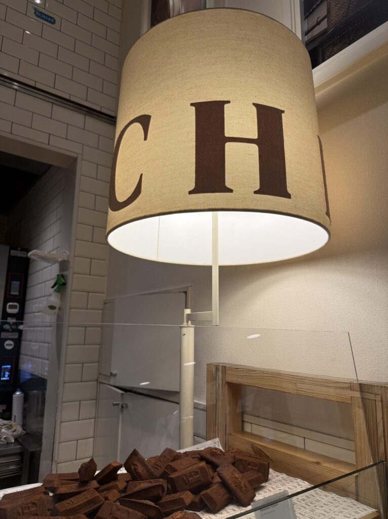 Deep golden brown financiers stacked behind the acrylic barrier under a large lampshade