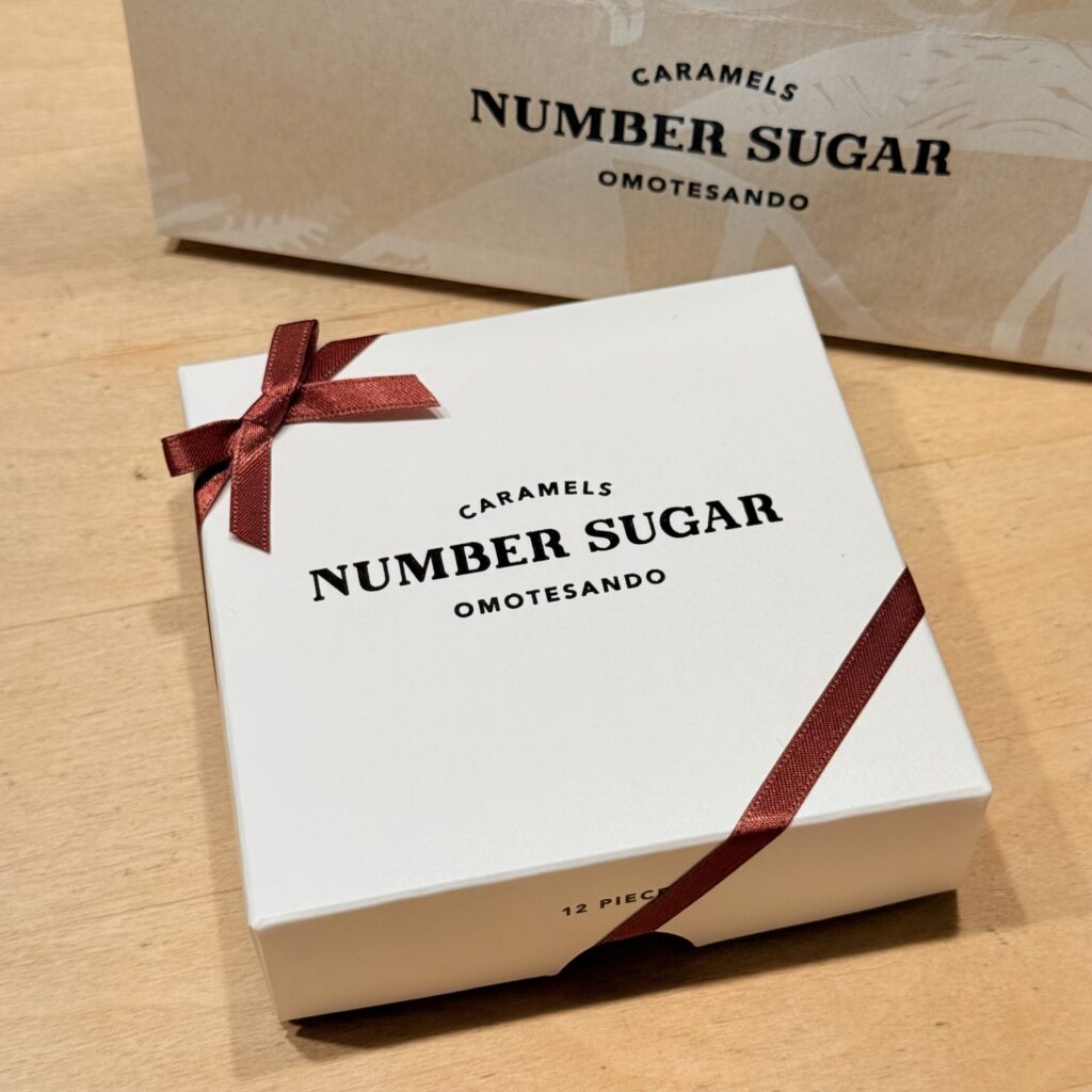 White 12-piece box with striking typography and a soft craft paper shopper bag behind it